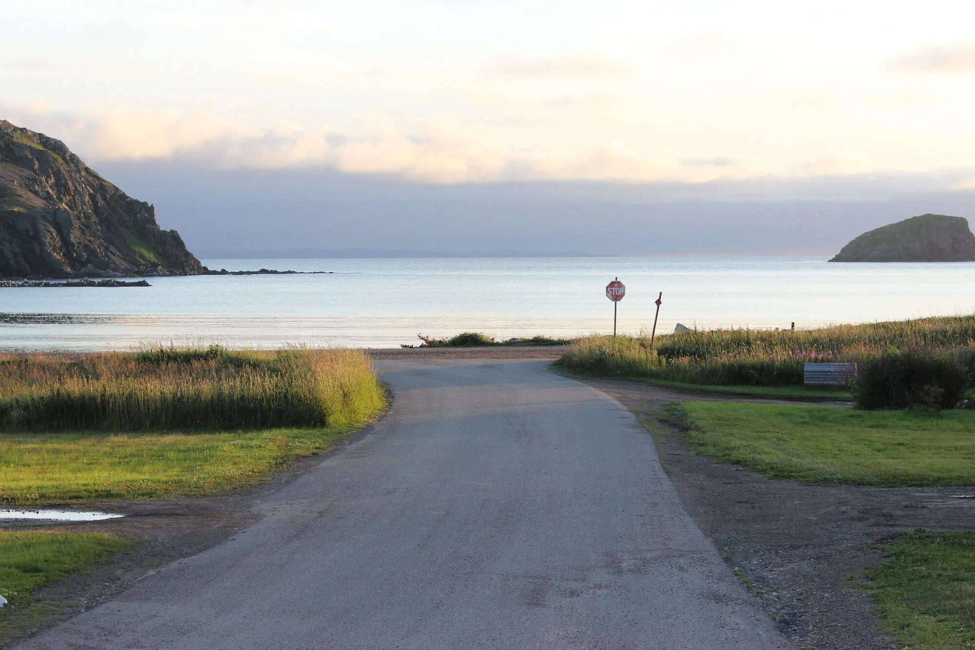 A quiet road running down to the shore of Back Harbour, Twillingate, a rocky headland beyond.