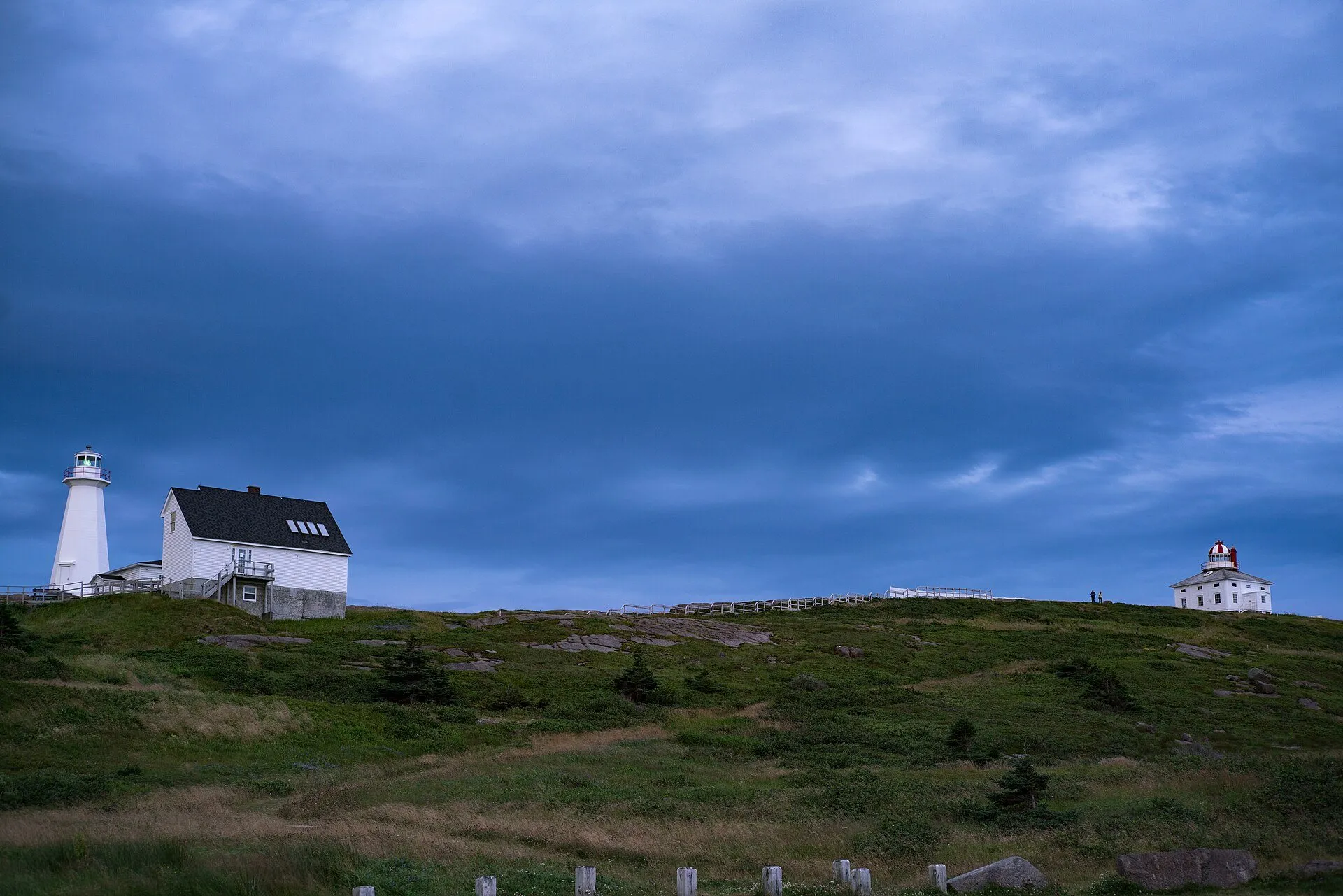 The square 1836 lighthouse with its lantern stands on the grassy headland at Cape Spear, with the newer white light tower and keeper's house to the left.
