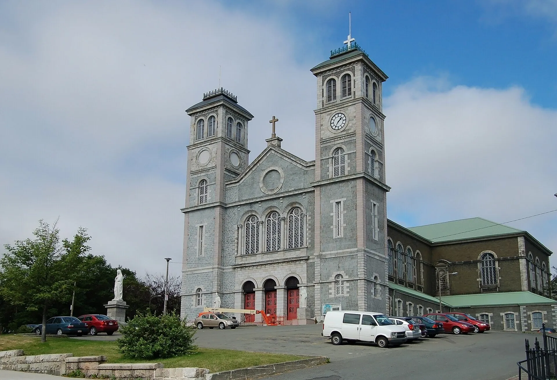 The grey stone Basilica of St. John the Baptist in St. John's with its twin clock towers and a statue on the lawn.