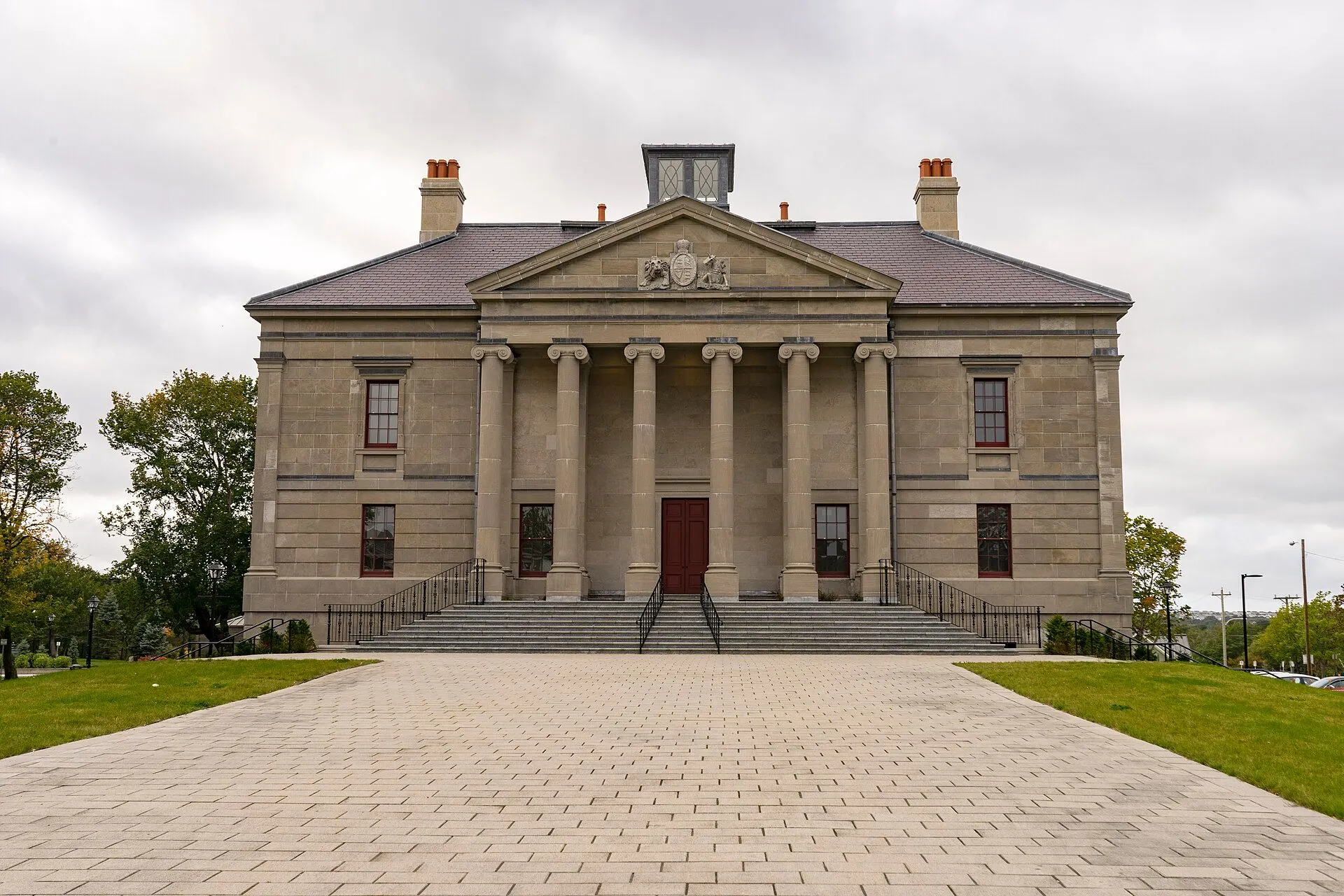 The Colonial Building's grey stone front with six columns and a pediment, seen up a paved walk in St. John's.