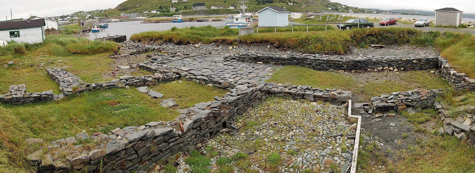 Excavated stone foundations of the 17th-century Colony of Avalon at Ferryland, with the harbour and houses behind.