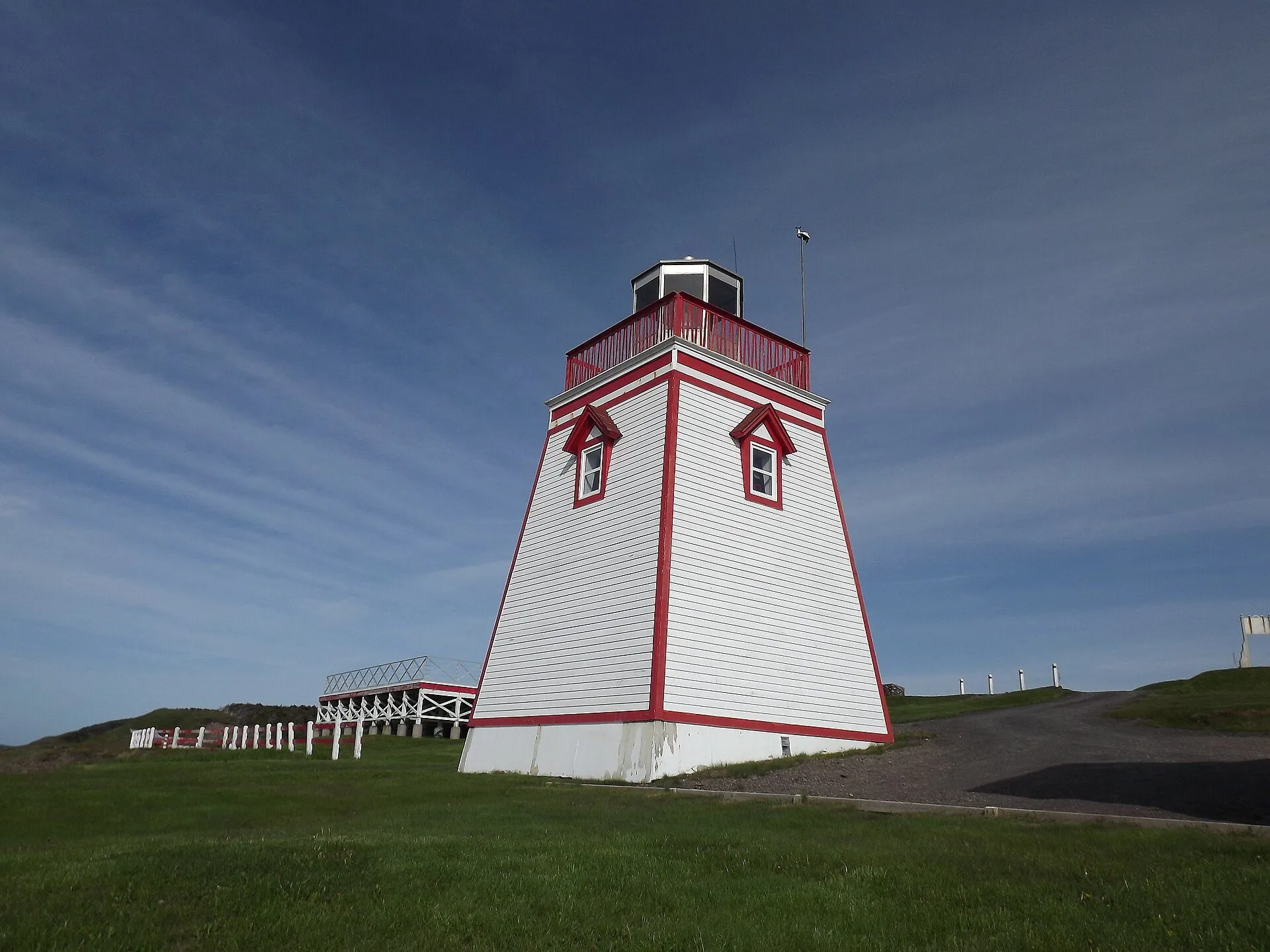 The white Fortune Head lighthouse with red trim stands on a grassy headland under a streaked blue sky.