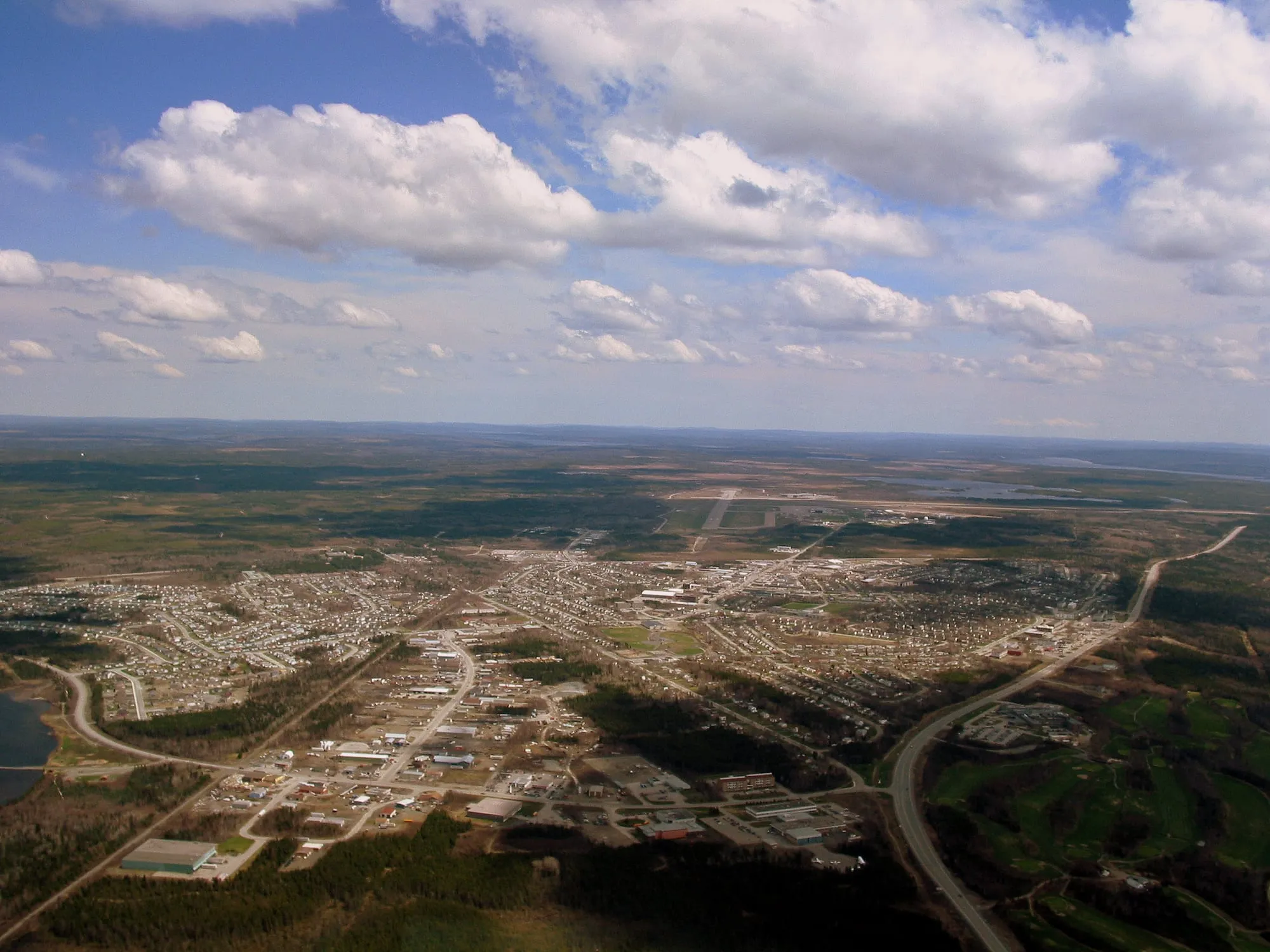 Gander from the air: the town's grid of streets in the forest, the Trans-Canada curving past, and the land running flat to the horizon.