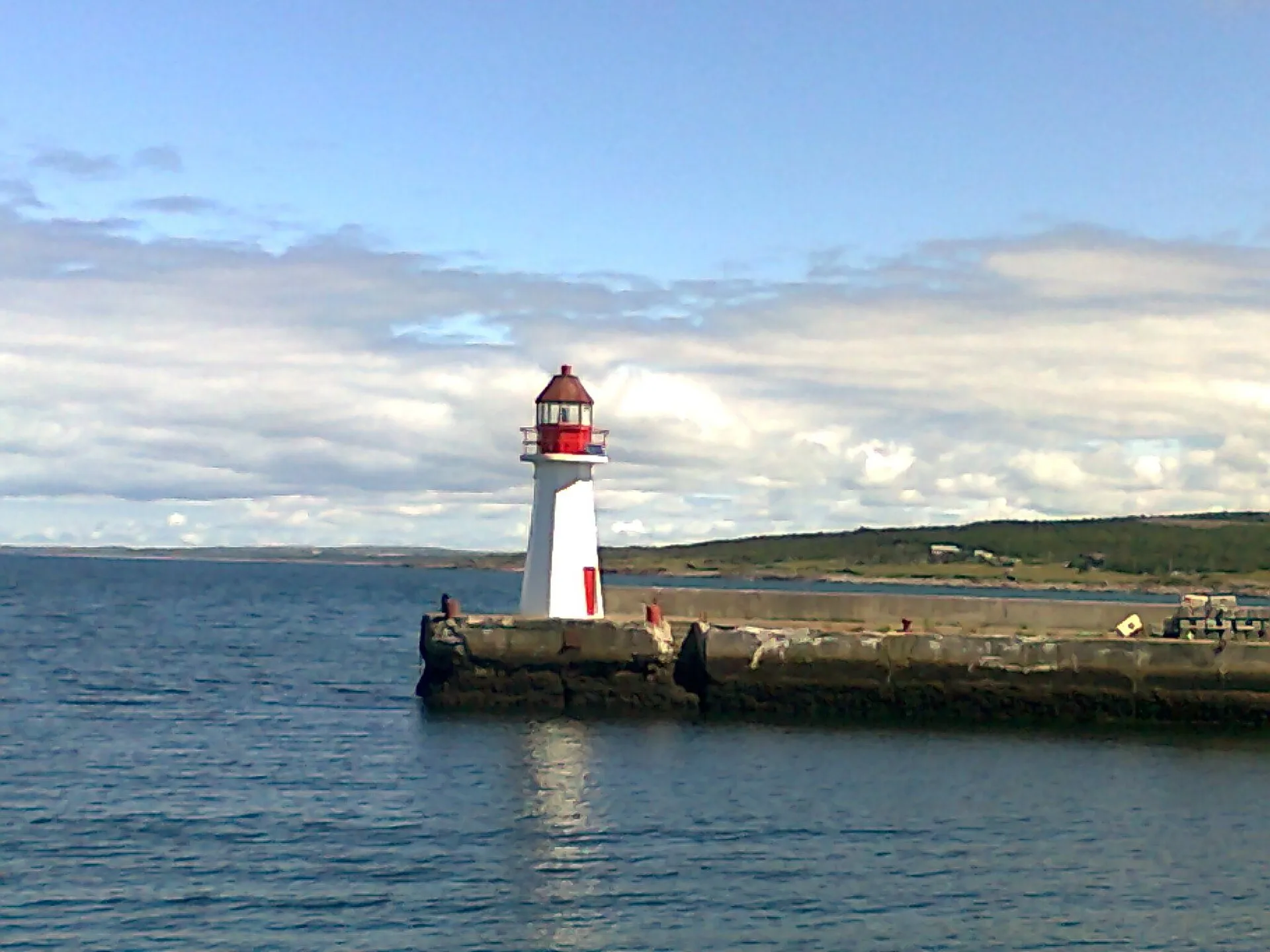 A white lighthouse with a red lantern at the end of a stone breakwater in Grand Bank harbour.