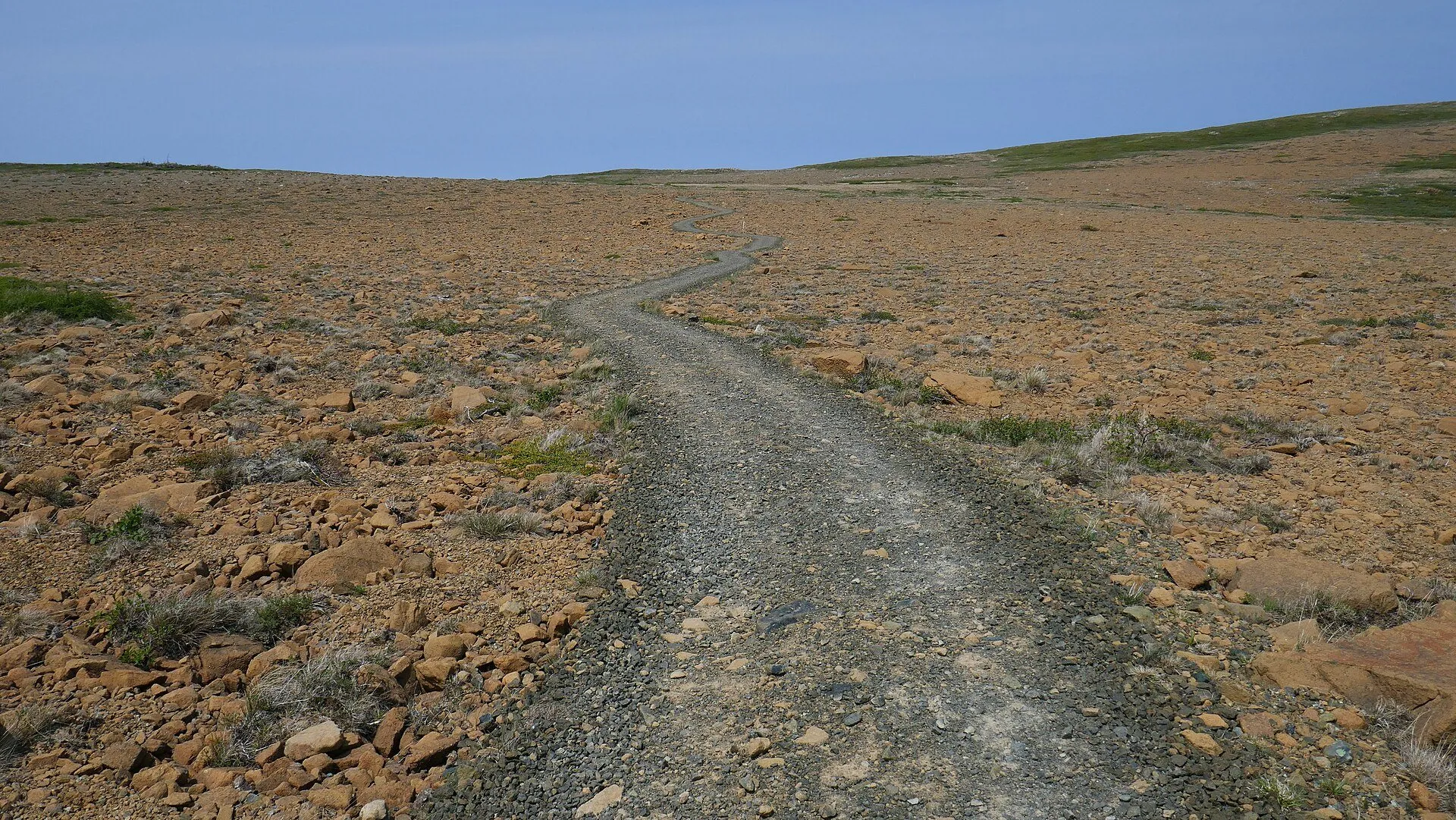 A gravel path runs across bare, rust-coloured serpentine barrens at the start of the Green Gardens trail.