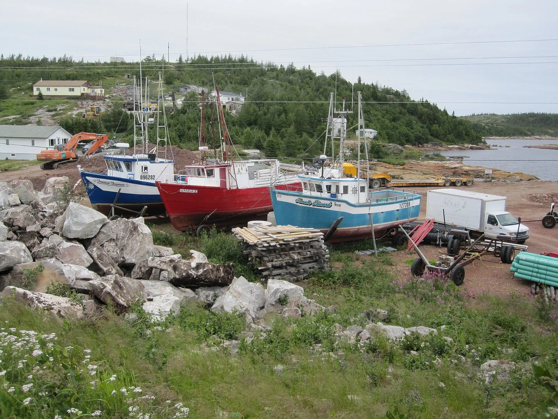 Fishing boats hauled up on the shore at Mary's Harbour, with houses and spruce hills behind.