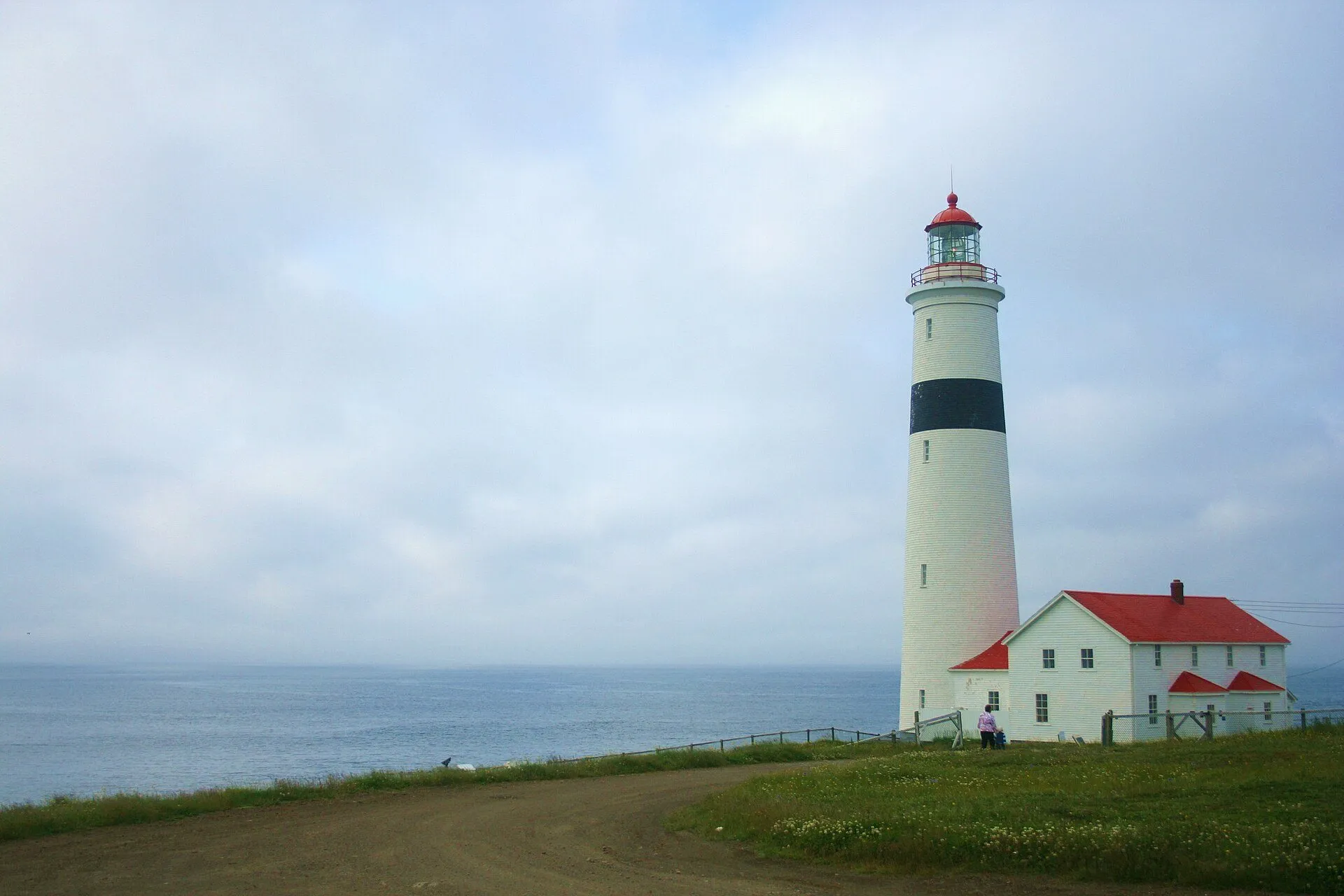 Point Amour Lighthouse, a tall white tower with a black band, beside its red-roofed keeper's house above the Strait.