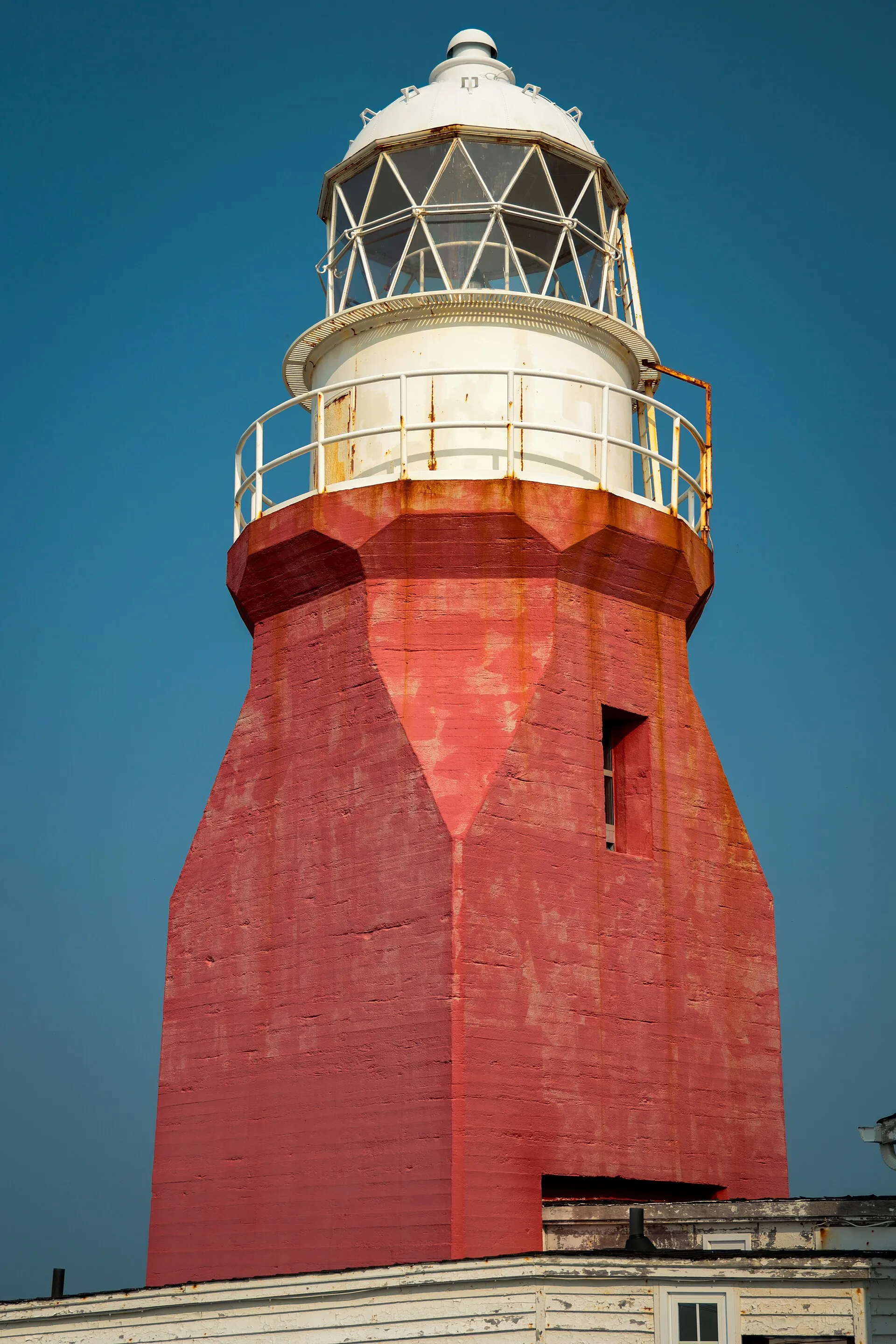 Long Point Lighthouse at Crow Head, Twillingate — the flared red concrete tower and white lantern against a clear sky.
