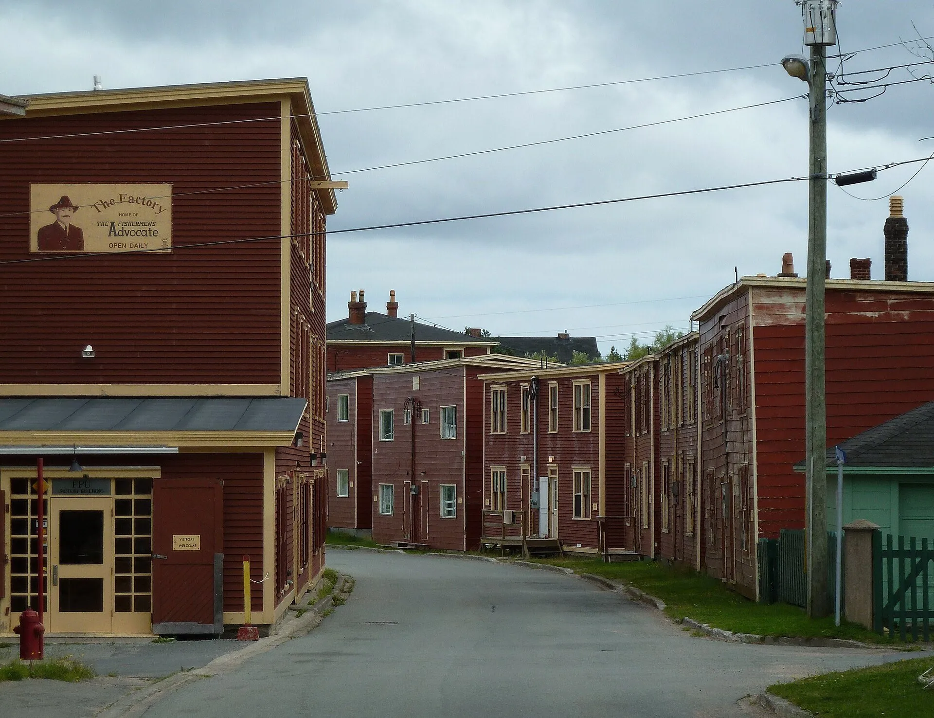 Rows of red clapboard buildings line a curving street in Port Union's historic district, with the Factory building on the left.