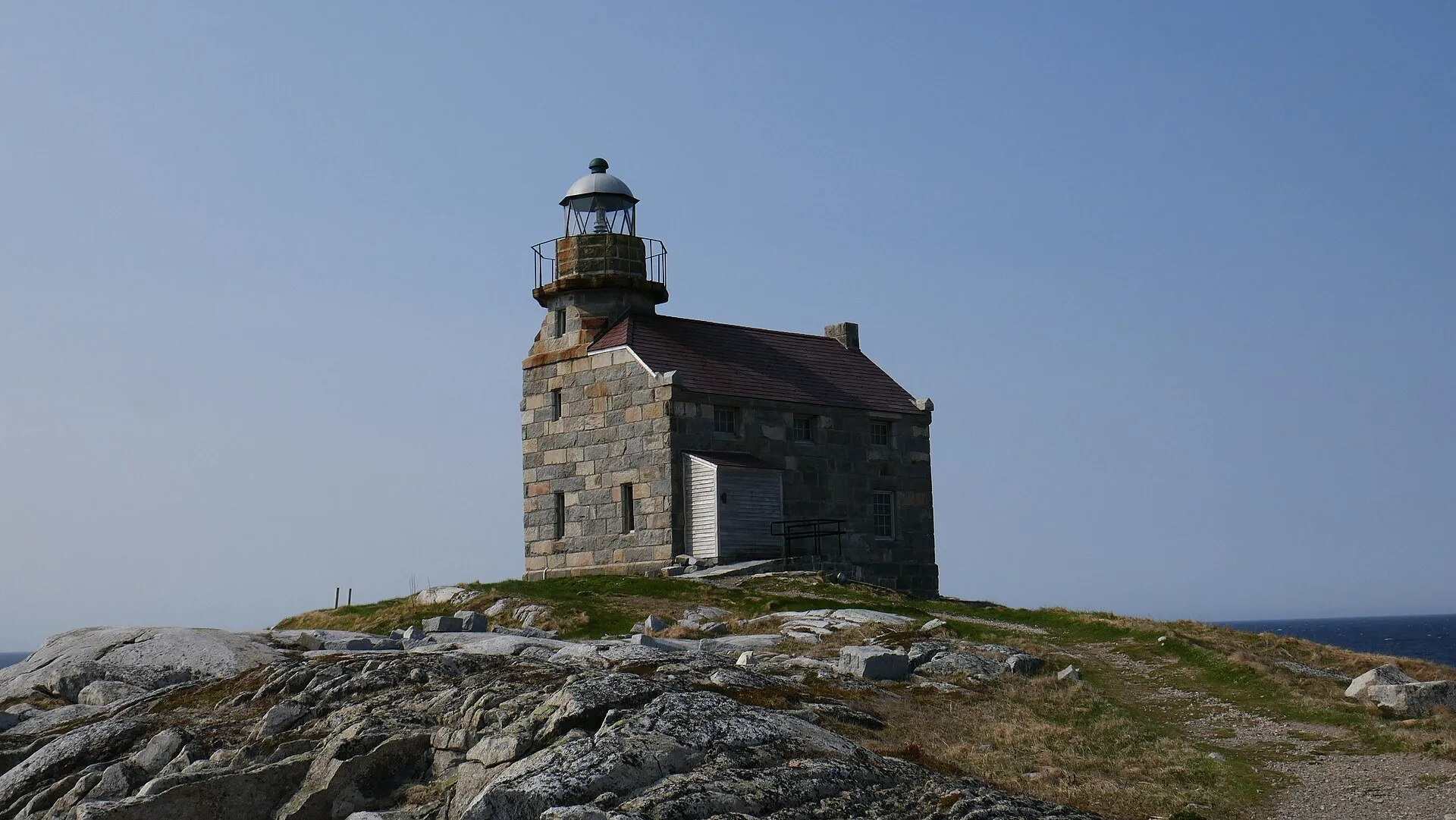 The granite Rose Blanche Lighthouse stands on a rocky knoll above the sea.