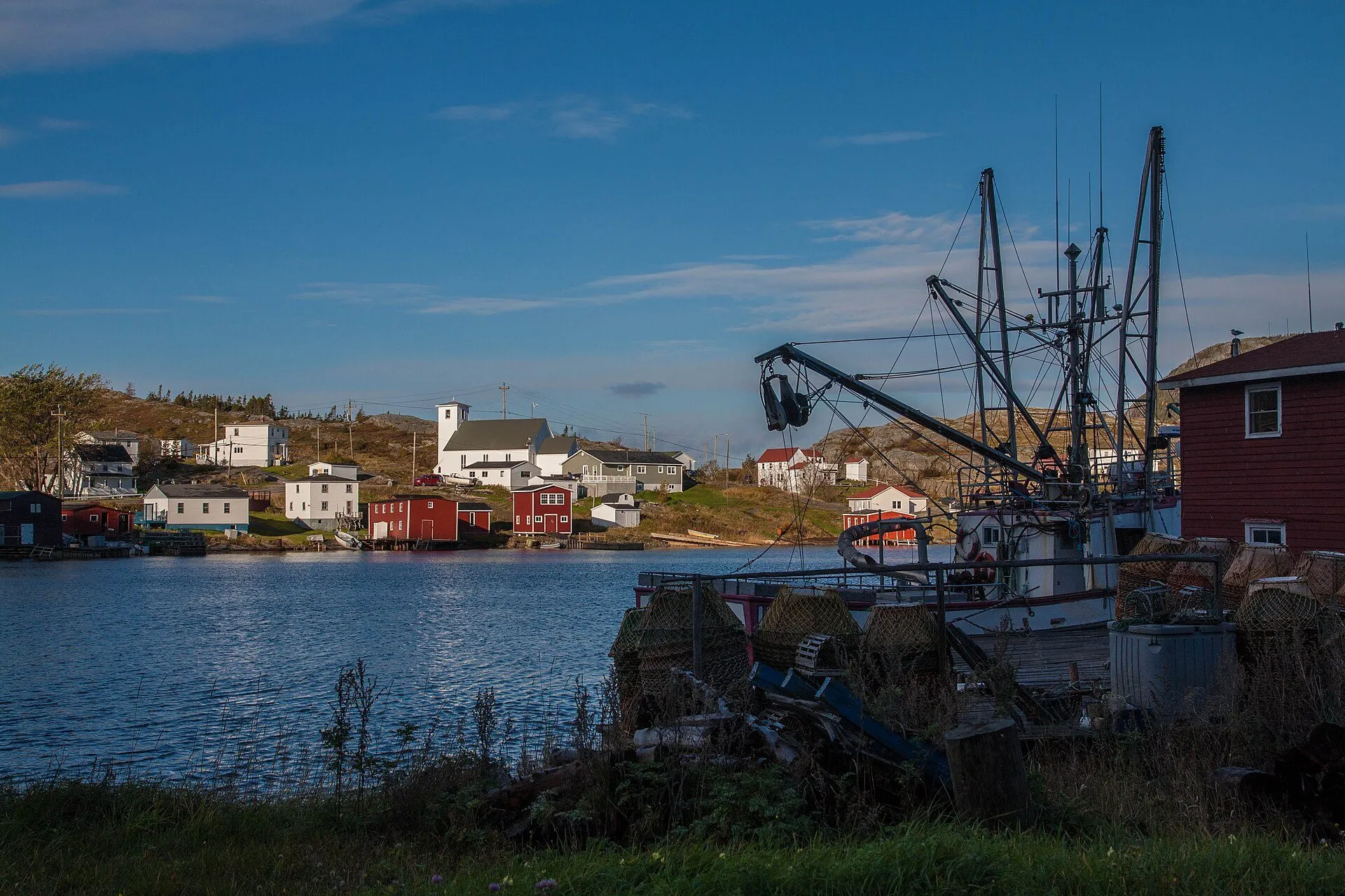 Fishing boats and stages sit along the harbour at Salvage, with white houses and a church on the far shore.