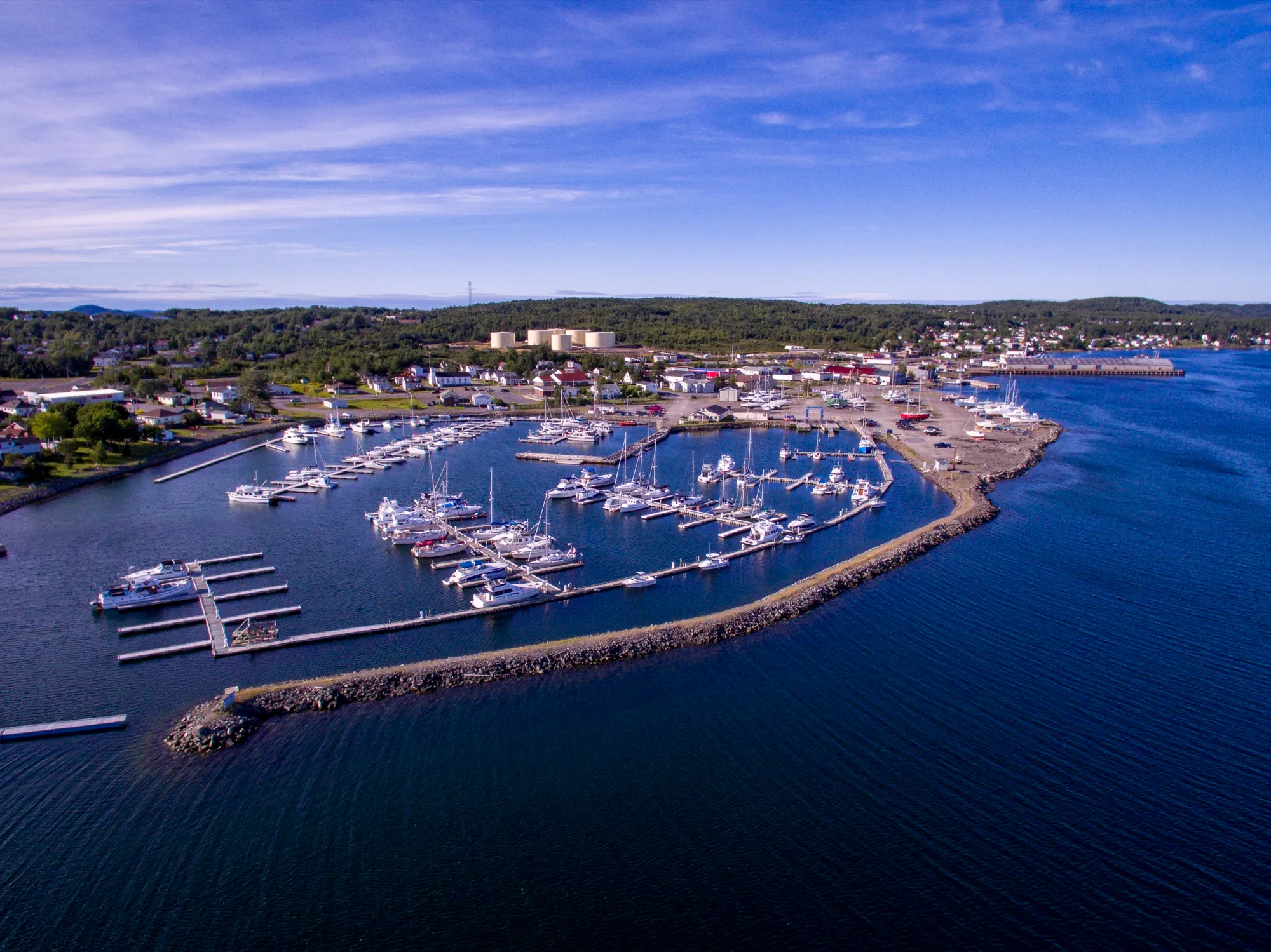 Aerial over Lewisporte's marina and breakwater with the town and Bay of Exploits behind, blue sky.